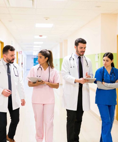 Male and female Hispanic healthcare workers discussing reports while walking in corridor at hospital